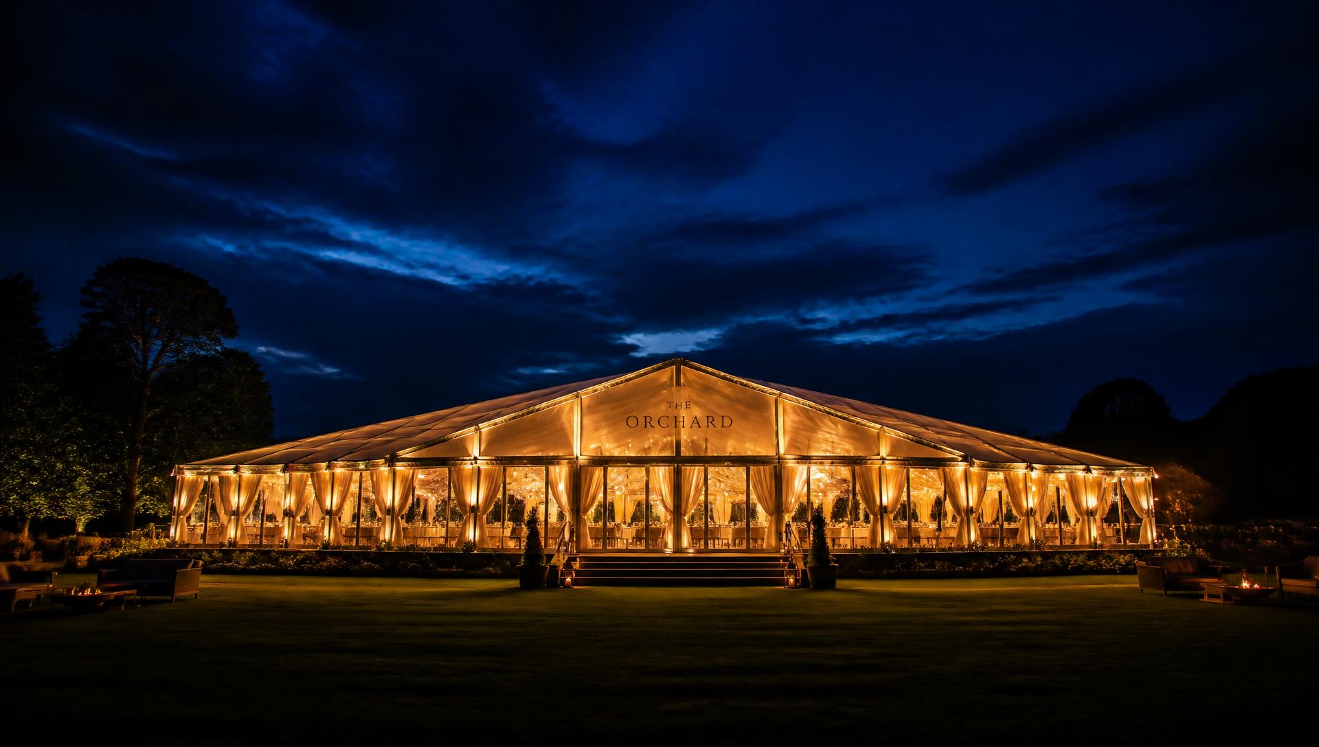 Illuminated marquee glowing on a lawn under a deep blue evening sky